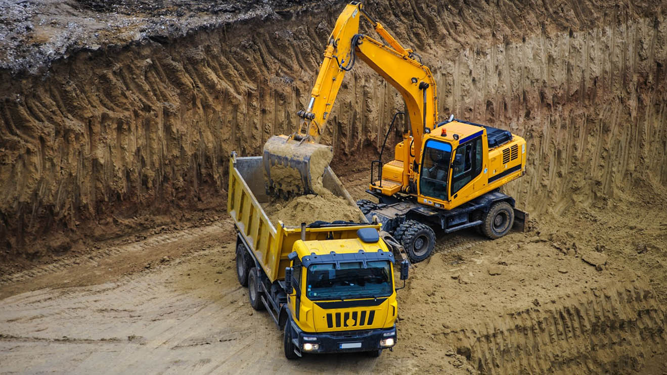 An excavator filling a dump truck with a load of dirt