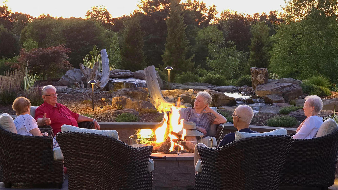 A group of elderly people sitting around a fire table talking