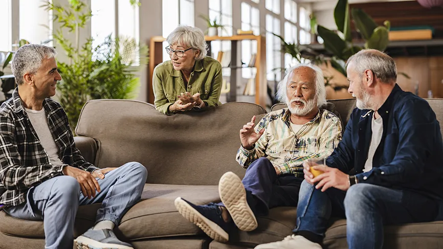 Four senior friends, including a woman and three men, engaging in a lively discussion while relaxing on a comfortable sofa in a modern living room