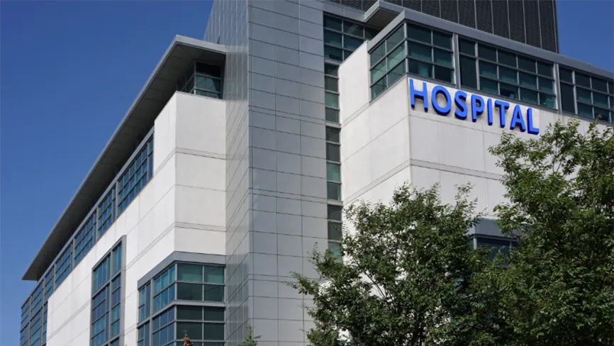 Modern hospital building in a suburban setting surrounded by trees.