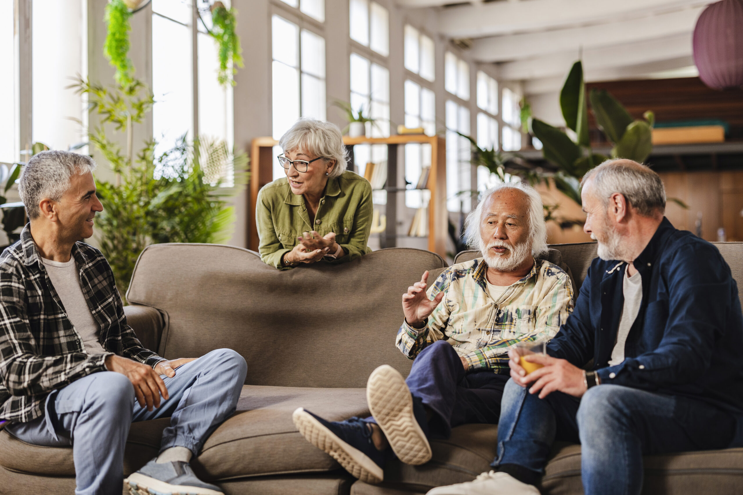 Four senior friends, including a woman and three men, engaging in a lively discussion while relaxing on a comfortable sofa in a modern living room